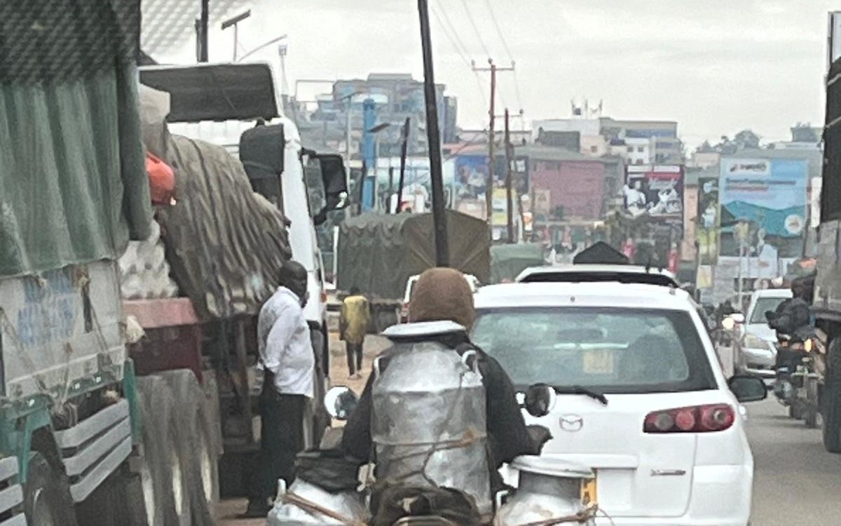 A boda-boda rider transporting aluminium milk cans through Kampala traffic